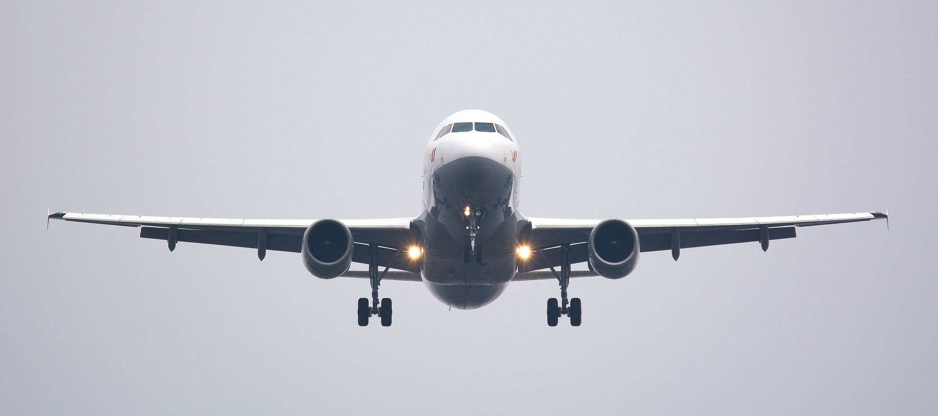 A commercial airliner captured head-on, preparing to land against a cloudy sky